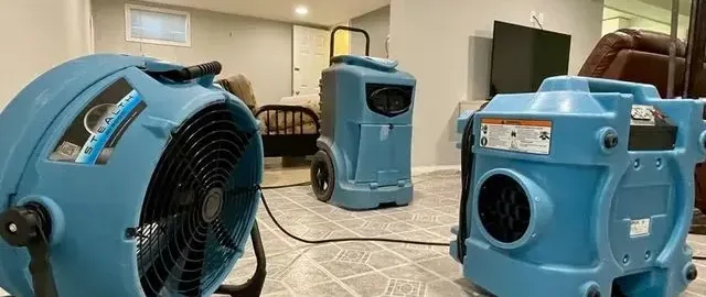 Air movers and a dehumidifier running in a room during drying after water damage