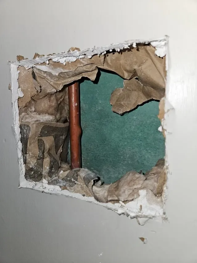 Drywall cut open to reach a leaking copper pipe inside the wall
