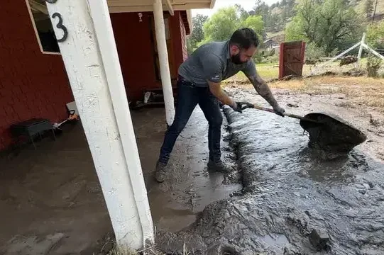 Man shoveling storm mud and runoff from under a carport after heavy rain