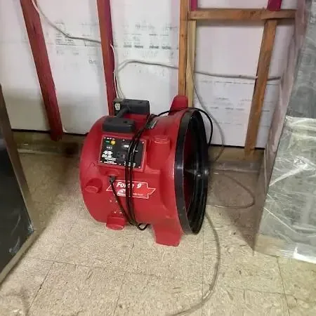 A red air mover drying a room where the lower wall is opened and plastic sheeting hangs