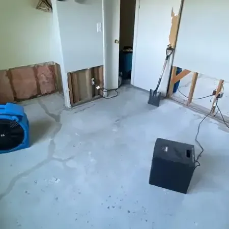 Air movers and a dehumidifier drying a room with the lower drywall removed and a bare floor