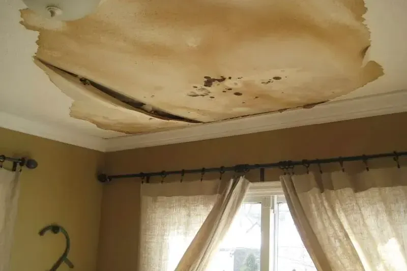 Sagging, water-stained ceiling drywall peeling above a curtained window