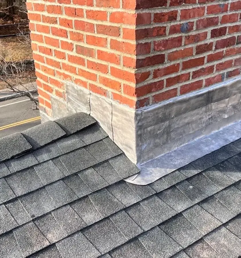 Metal flashing at the joint between a brick chimney and an asphalt shingle roof