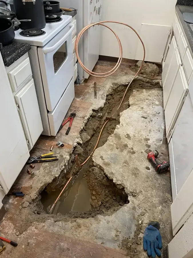 A kitchen floor cut open in a trench to reach a leaking copper line beneath the slab