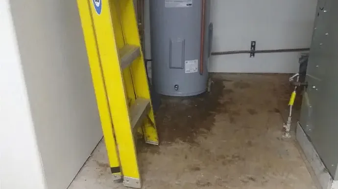 A water heater in a utility closet with leaked water across the floor
